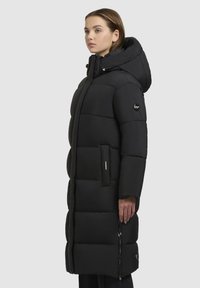 Sorte pufferjakke med hætte, der har en quiltet design, lynlåslommer på siden og en lige silhuet, lavet af slidstærkt stof.