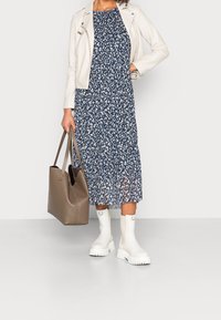 Granatowa sukienka z białymi wzorami, warstwowym dołem; kremowa skórzana kurtka motocyklowa; beżowa torba na ramię; białe botki na grubej podeszwie.