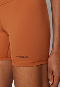 Rudos sportiniai šortai, pagaminti iš tamprios, lygaus audinio. Ant apatinio krašto yra juodas Puma logotipas ir sustiprinti siūlai.