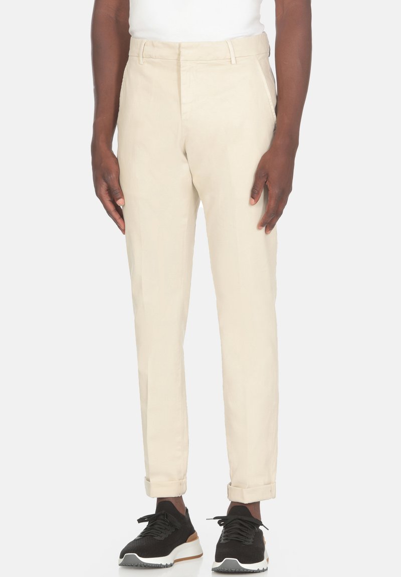 Pantaloni in cotone beige dal taglio slim, con frontale piatto, risvolti e tasche laterali, abbinati a scarpe da ginnastica nere.