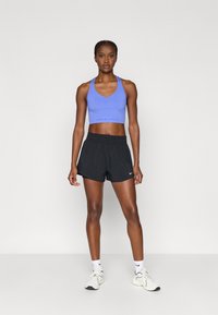 Nike Pro sport-bh i lyseblå med v-hals og matchende elastikbånd, kombineret med sorte træningsshorts med logo.