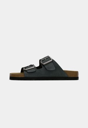 Sort sandal med to stropper og justerbare spænder, korkfodseng og tekstureret gummisål. Simpelt design med åben tå.