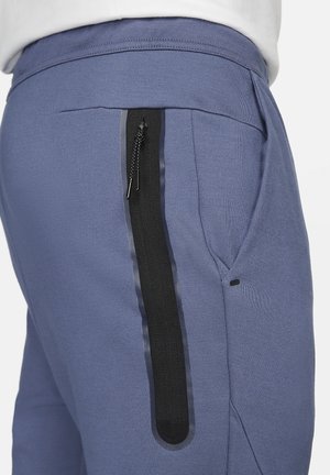 Blue sweatpants with a textured fabric, featuring a black zippered pocket on the side and a stretchy waistband for comfort.
