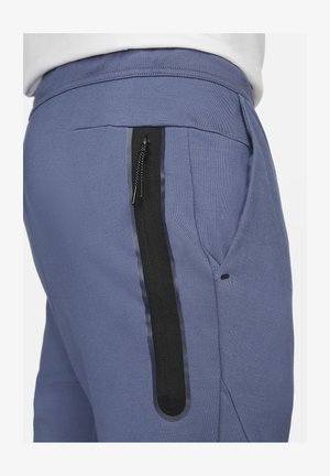 Pantalon de survêtement bleu en tissu texturé, avec une poche zippée noire sur le côté et une ceinture extensible pour plus de confort.