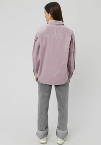 Chemise en velours côtelé à manches longues de couleur violet clair, avec un col, des manches boutonnées et une coupe décontractée. Assortie avec un jean évasé gris clair.