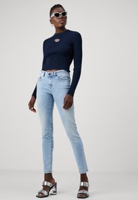 Marinblå rippad croppad topp, ljusblå slim-fit jeans och metalliska klacksandaler. Accessoarer inkluderar vita kattögon-solglasögon och hoop örhängen.