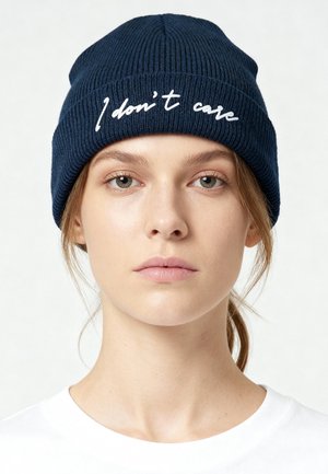 Navy knit beanie with ribbed texture and embroidered white text "I don't care" on the front, featuring a snug, tapered design.