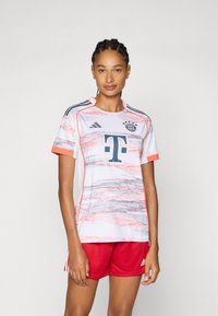 Maglietta da calcio bianca con motivo a pennellate rosa e grigie, caratterizzata da un collo rotondo, maniche corte e dettagli del logo. Abbinata a pantaloni corti rossi.