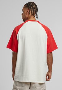 Red and white short-sleeve t-shirt with a raglan design. Made of cotton, featuring a smooth texture and loose fit.