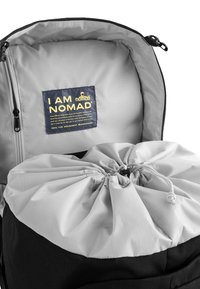Zwart en grijs rugzak interieur met een grijze trekkoordsluiting, contrasterende stoftexturen en een logopatch met de tekst "I AM NOMAD."