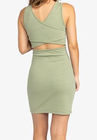 Zelené upnuté šaty s texturovanou tkaninou, s překříženým designem na zádech a malým akcentním knoflíkem, zdůrazňující výřez v pase.