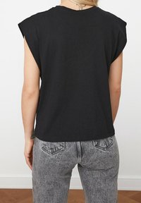 Sort bomulds ærmeløs top med let afrundede skuldre, sammen med højtaljede lyse grå jeans med baglommer og subtil tekstur.