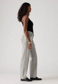 Zwarte mouwloze bodysuit, lichtgrijze high-waisted jeans, getailleerde pasvorm, wijde pijpen, subtiele stikseldetails, gedragen met zwarte schoenen.