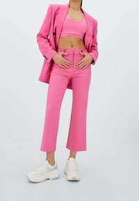 Heldere roze getailleerde blazer en bijpassende crop top, gecombineerd met licht flared roze broeken. Witte sneakers met neutrale accenten.