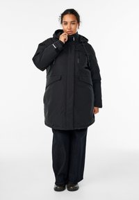 Crni dugi kaput s kapuljačom, s prednjim patentnim zatvaračem, podešivim vezicama i dva velika prednja džepa. Nositi preko tamnih traperica i cipela.