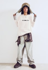 Cămașă crem cu mânecă lungă, cu imprimeu "HOME ALONE", asociată cu o cămașă din flanel cu carouri legată în jurul taliei, pantaloni din catifea, și cizme negre cu platformă. Pălărie căptușită cu blană.