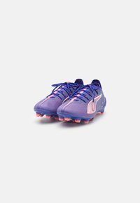 Des crampons de football violets avec des accents roses, en matériau texturé et avec des crampons moulés pour une traction ; dotés de lacets et d'un logo sur le côté.
