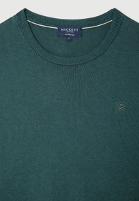 Pull vert en mélange coton-soie avec un col ras du cou, des poignets côtelés et un petit logo brodé sur la poitrine. Finition légère et texturée.