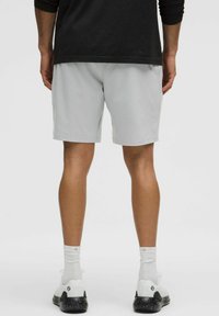 Šviesiai pilki sportiniai šortai, pagaminti iš kvėpuojančios medžiagos, su laisvu kirpimu. Dėvimi su baltais kojiniais ir sportbačiais su juodais akcentais.