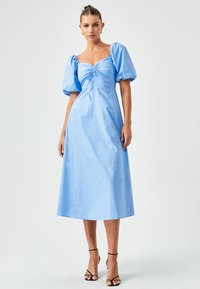 Heleda sinine, põlvepikkune puuvillane kleit, millel on puffpoolsed varrukad, ruudukujuline kaelus ja esine nööriga detail. Minimalistlik riistvara.