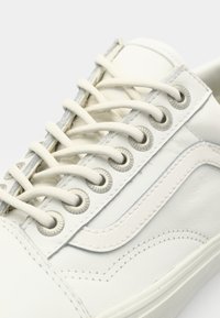 White leather sneaker with rounded toe, silver eyelets, and flat laces. Features a textured side stripe and stitched detailing.