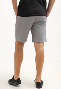 Grijze shorts van een gladde, lichte stof, met een ontspannen pasvorm en zijzakken. Draagt met zwarte sneakers.