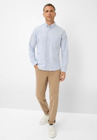 Lichtblauw, gestreept overhemd met kraag; gecombineerd met tan chino's en witte sneakers. Voorzien van een enkele borstzak.