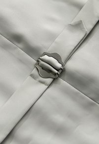 Tissu gris à la texture lisse, présentant un fermoir en métal argenté proéminent. Le design comprend des sections cousues pour plus de détail.