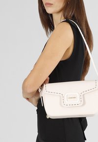 Borsa a mano in pelle rosa chiaro con un design strutturato, caratterizzata da cuciture decorative e un accento in metallo dorato sul davanti.
