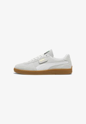 Weiße Wildleder-Sneaker mit einem hellgrauen Overlay, ausgestattet mit einer strukturierten Gummisohle und einem kleinen grün-schwarzen Etikett auf der Zunge.