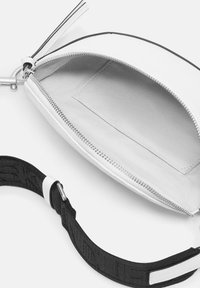 Biała torba materiałowa z suwakiem w kolorze srebrnym i czarnym paskiem, z gładką powierzchnią, wewnętrzną kieszenią i minimalistycznymi elementami projektu.