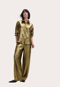 Conjunto de dos piezas en oro metálico que incluye una camisa abotonada con mangas remangadas y pantalones de pierna ancha; textura suave y ajuste holgado.