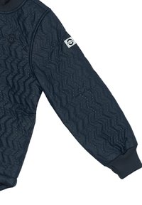 Mornarska šivača majica s teksturiranim zigzag vzorcem in majhnimi okrasnimi žebljički. Ima rebraste manšete in logotip prišiten na rokavu.