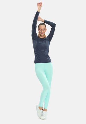 Navy long-sleeve athletic top paired with mint green leggings and white sneakers. The top has a smooth texture; the leggings are fitted.
