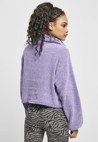 Pull cropped violet avec une texture côtelée et un col haut replié. Associé à un pantalon gris avec un motif zébré noir.