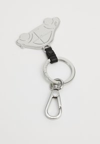Porte-clés en métal avec un charme en forme de voiture, finition argentée avec des détails gravés, attaché à une sangle en cuir noir et un anneau circulaire.
