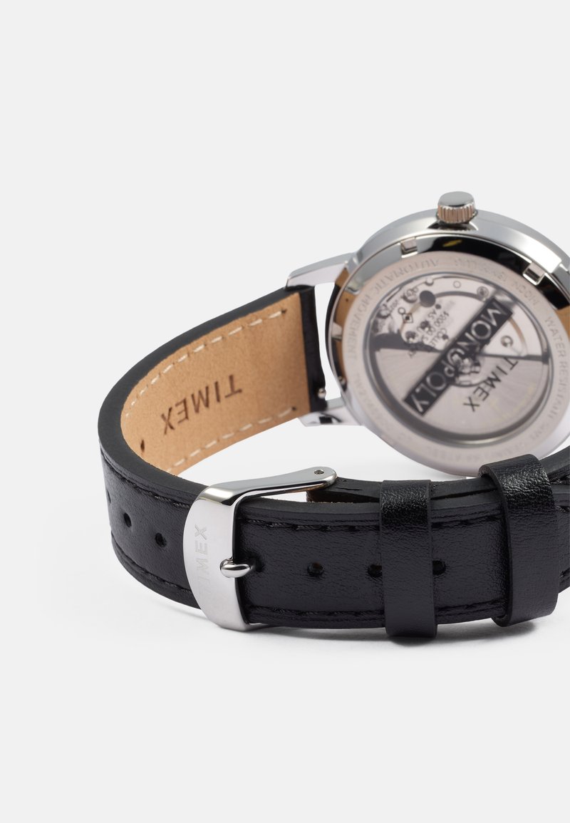 Reloj con correa de piel negra y herrajes de acero inoxidable plateado, que presenta una caja trasera transparente que muestra el movimiento.