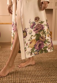 Kimono in seta floreale con sfondo crema, caratterizzato da rose e foglie multicolori, spacco a lunghezza ginocchio e bordi a contrasto viola.