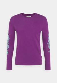 Violetti pitkähiha -paita, joka on valmistettu puuvillasta. Vasemmassa hihassa on tealvärinen koristeellinen muotoilu. Pyöreä kaula-aukko ja normaali mitoitus.