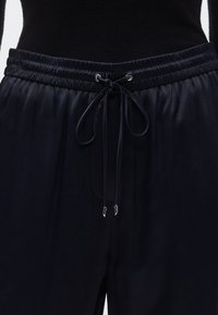 Tumši zili sporta legingi ar elastīgu jostasvietu, auklu aizdari un metāliskām galiņām. Gluda tekstūra ar vieglu spīdumu.