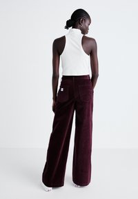 Witte geribbelde mouwloze top gecombineerd met burgundy wijdvallende corduroy broek met achterzakken en een merklabel.