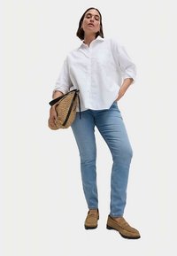 Vit skjorta med knappar, ljusblå jeans, bruna skor, håller en stråväska med svart rem. Rena linjer och avslappnad passform.