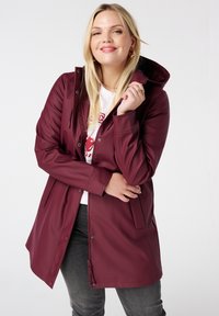 Veste imperméable bordeaux avec capuche, fermeture à bouton à l'avant et cordon de serrage ajustable à la taille. Dispose de poches latérales et d'une finition lisse.
