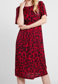 Punainen mekko mustalla leopardikuviolla. Lyhyet hihat, pyöreä pääntie, polvipituinen, valmistettu sileästä kankaasta. Hieman levenevä siluetti.