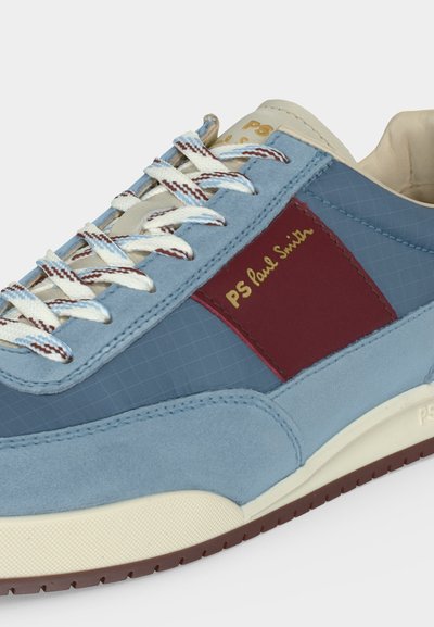 Ανοιχτό μπλε αθλητικό παπούτσι με λευκά και καφέ κορδόνια, μαρονού πλευρικό πάνελ, μπεζ σόλα και το «PS Paul Smith» κεντημένο με χρυσά γράμματα.