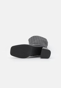 Botte noire matelassée jusqu'au genou avec un extérieur texturé, un talon bloc et une semelle en caoutchouc présentant un motif de grip diagonal.