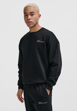 Zwarte sweatshirt van zachte stof, met een ronde halslijn en een grafische print op de borst. Gecombineerd met bijpassende zwarte broek.