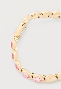 Χρυσό βραχιόλι με ροζ πολύτιμους λίθους σε σχήμα δάκρυου που συνδέονται με γυαλιστερά χρυσά στοιχεία σε ανοιχτό φόντο.