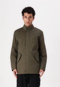 Olive green jacket made of smooth fabric, featuring a high collar, snap button closure, and side pockets. Straight cut, minimal design.