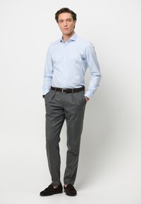 Lichtblauw overhemd met knopen, grijze gestructureerde broek, zwarte leren riem en donkere loafers. Formele outfit met een getailleerde pasvorm.